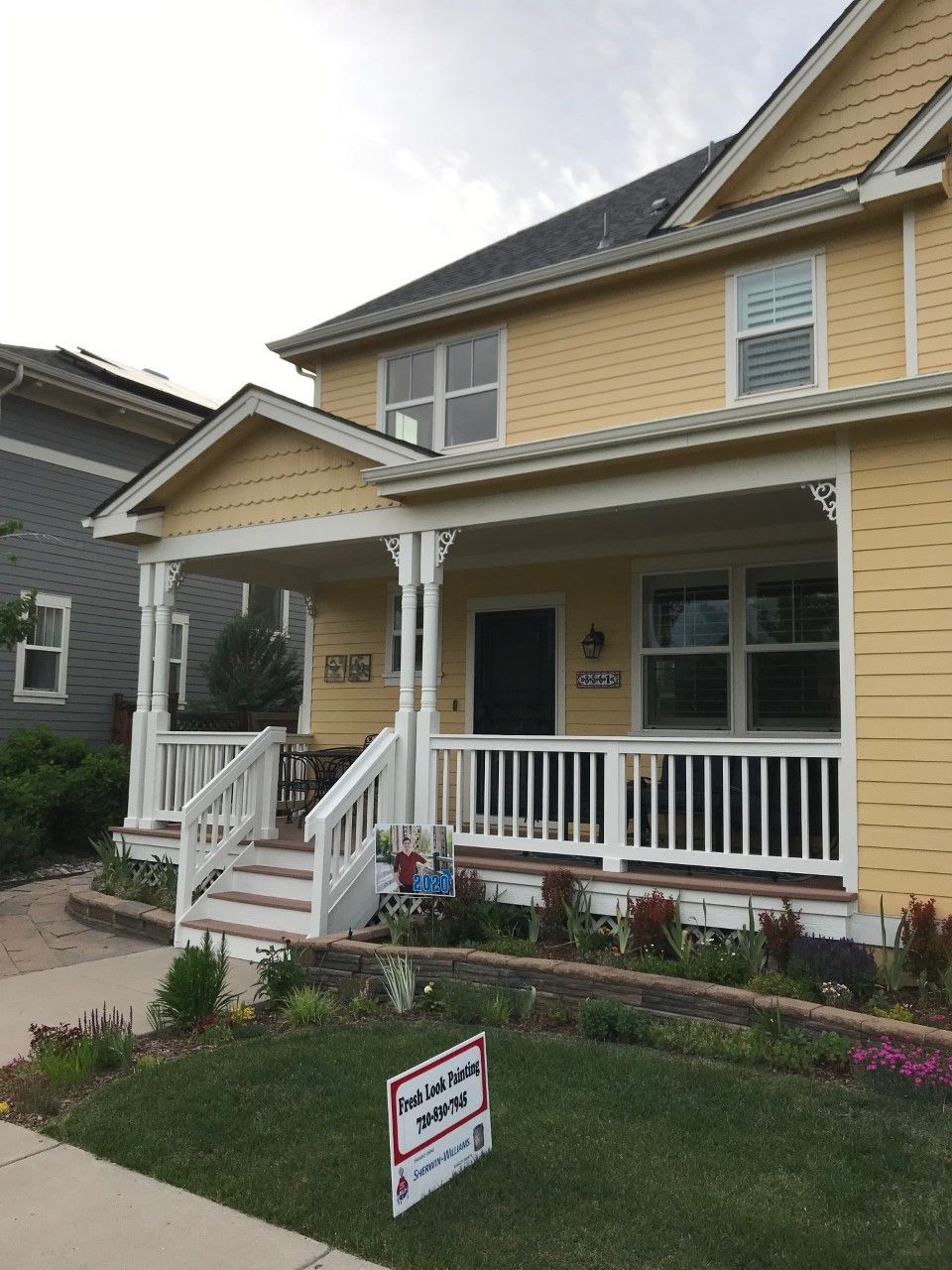 Yellow house with white porch and railings; small flower garden in front yard.