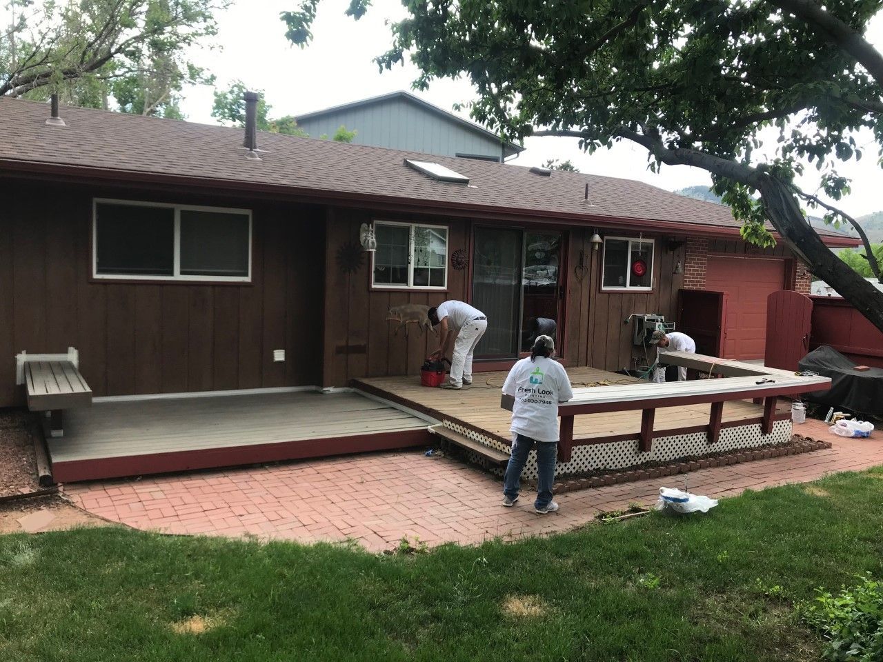 Workers building a wooden deck in a backyard beside a brown house