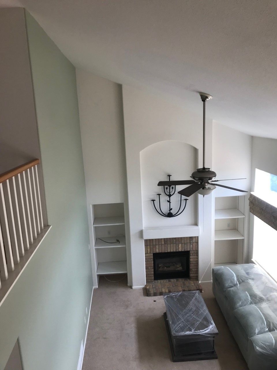 High-angle shot of a living room with vaulted ceiling, fireplace, built-in shelves, and a ceiling fan.
