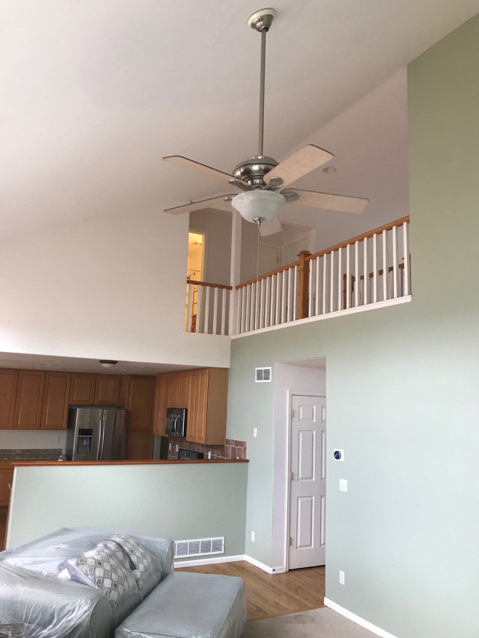 Living room with vaulted ceiling, ceiling fan, loft railing, kitchen pass-through, and light green walls