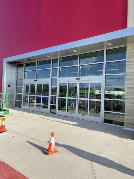 Glass storefront entrance with red facade and orange traffic cones on a sunny sidewalk