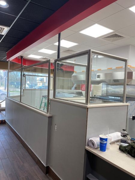 Empty cafeteria service counter with glass partitions, red ceiling trim, and a drink cup on the counter.