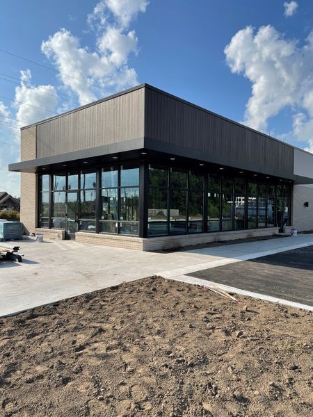 Modern glass storefront building with dark trim and paved walkway under clear sky