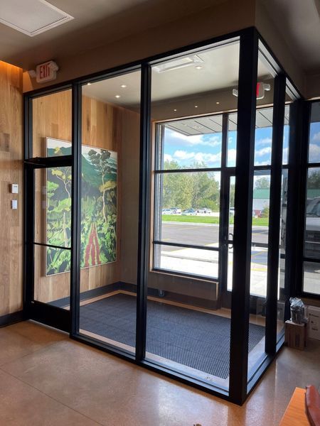 Glass entry vestibule with black-framed doors and a mural, viewed from inside a building.