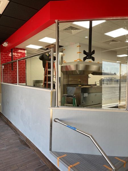Fast-food counter with stainless equipment behind glass, red-and-white interior, and metal handrail in foreground