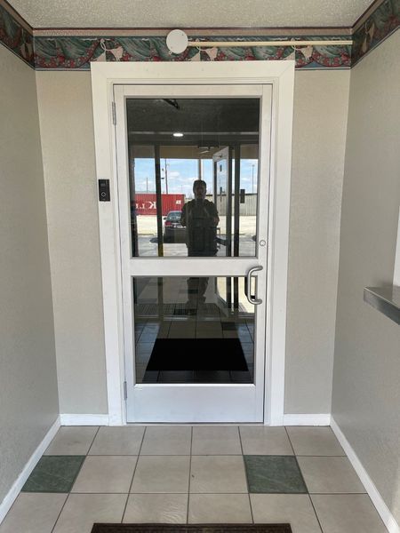 Glass entrance door in a tiled hallway, with a person reflected in the door.