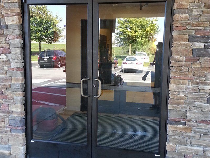 Glass double doors with metal handles in a stone storefront entrance, reflecting parked cars outside.