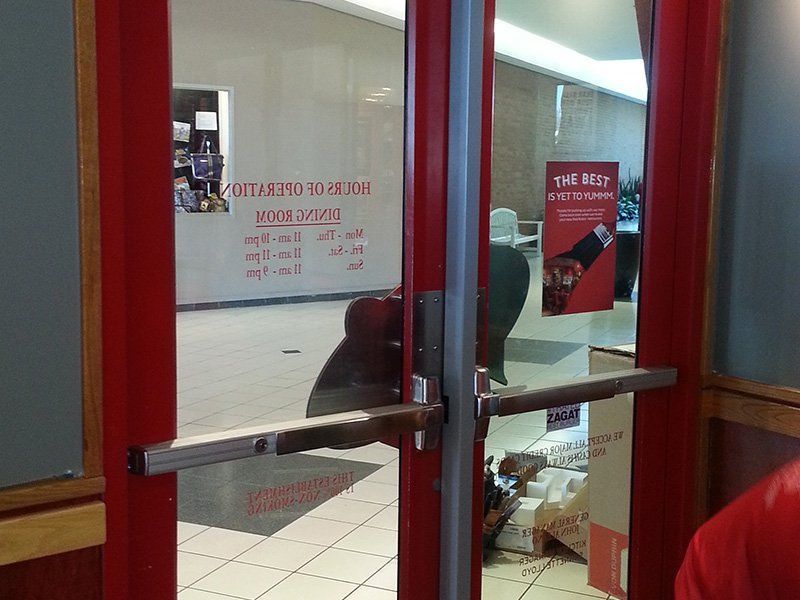 Red-framed glass doors to a store entrance, with a person bending near the doorway inside.