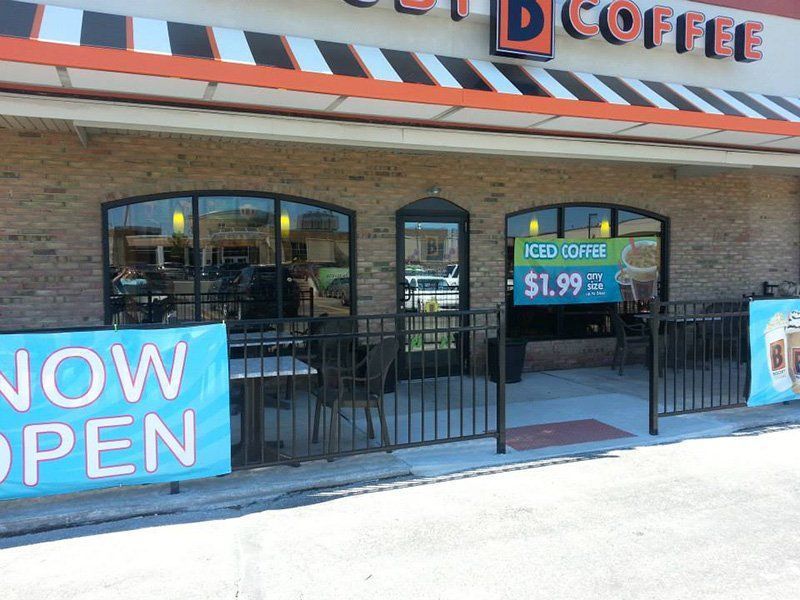 Coffee shop storefront with “Now Open” sign and iced coffee promo banner