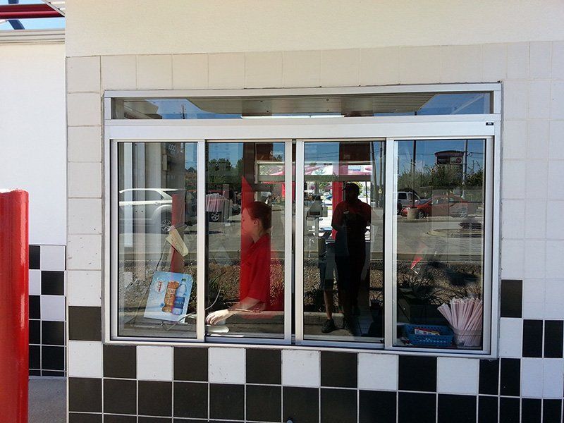 Fast-food restaurant drive-thru window with staff inside and a black-and-white tiled exterior