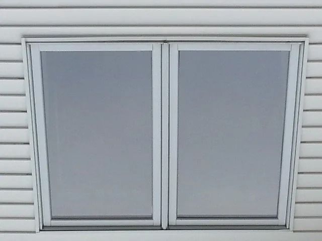 Closed white-framed window with gray blinds on a light siding wall