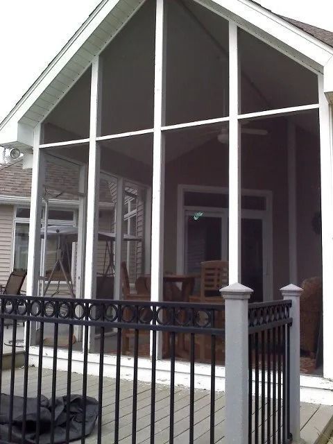 Front porch with black railing and tall white columns on a house with a steep gabled roof.