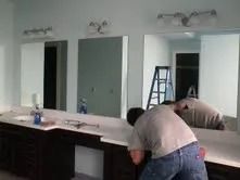 Worker leaning over a long bathroom vanity with mirrors and lights during renovation