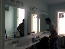 Person standing at a bathroom sink with mirrors, looking down while using the counter.