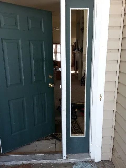Open front door with narrow sidelight window beside beige siding and porch steps