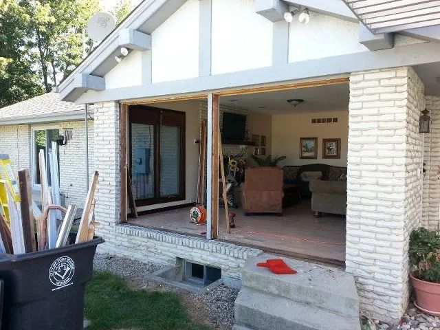 Patio entry with open sliding doors, stone columns, a bench, and a black bin in the foreground