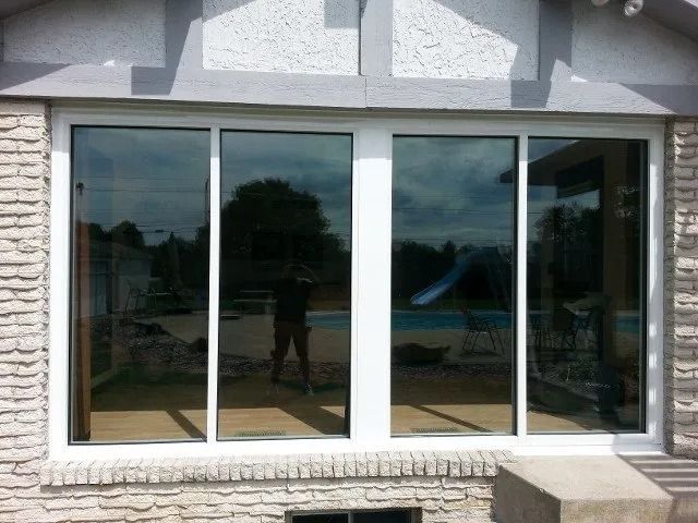 Large sliding glass window with white frame set in a stone facade, reflecting the outdoor yard.