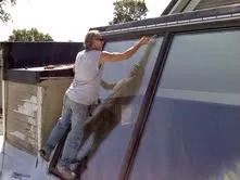 Man cleaning a slanted skylight on a rooftop with a long squeegee