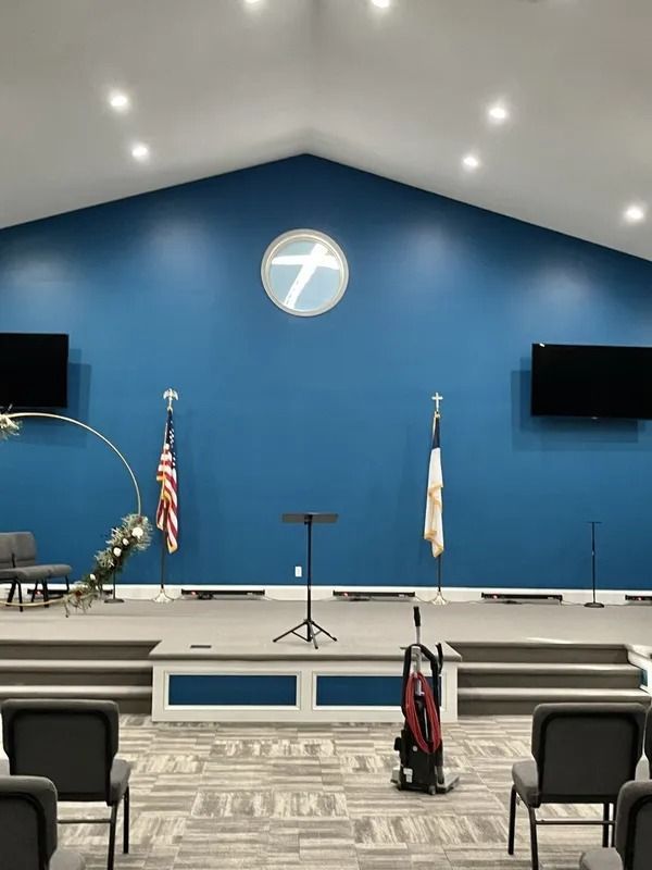 Church stage with blue wall, cross logo, podium, flags, and two wall-mounted screens