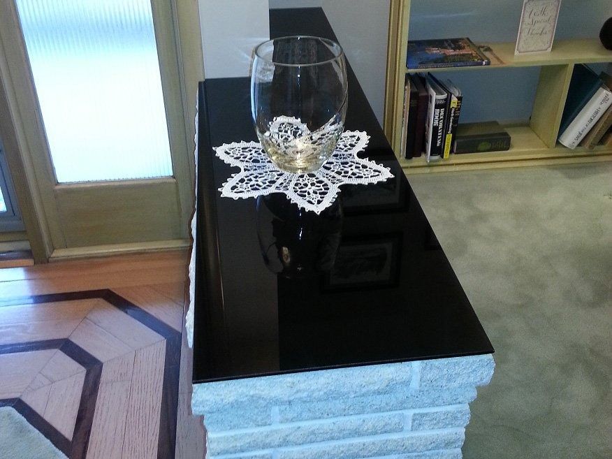 Black glossy console table with a wine glass on a white doily in a living room.