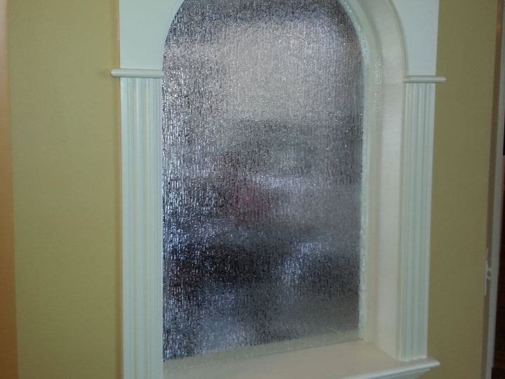 Frosted arched window with white trim and textured glass on a beige wall