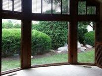 Large wood-framed windows overlook a green garden with hedges and white stones.