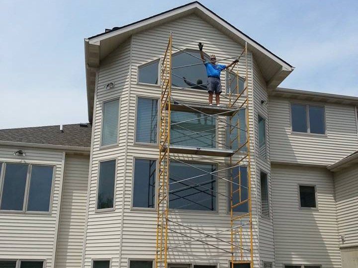 Worker on tall ladder painting a beige house exterior near the roofline