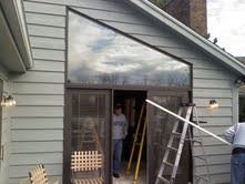Two workers installing a large glass door in a light gray house exterior