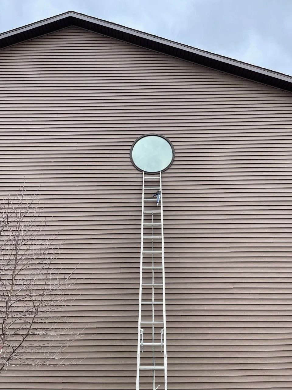A tall ladder leans against a house wall beneath a round window.