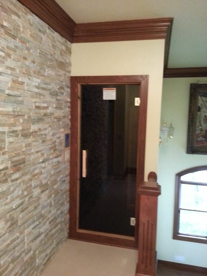 Interior view of a sauna door with dark glass, stone wall, and wood trim beside a stair railing
