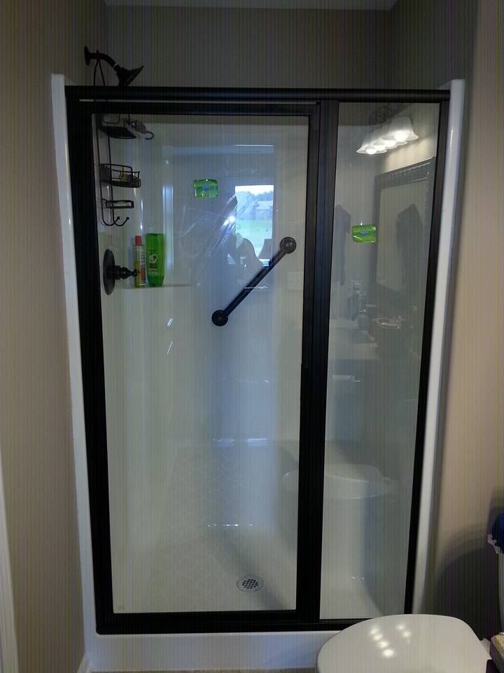Black-framed glass shower enclosure with sliding door and diagonal handle in a bathroom.