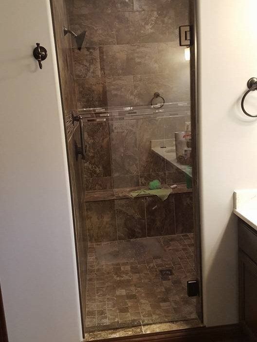 Small tiled walk-in shower with glass door and beige stone walls in a bathroom.