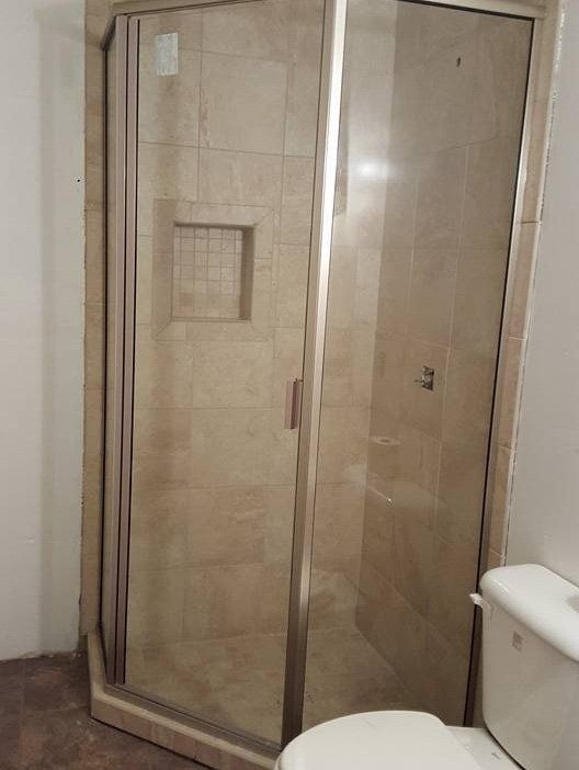 Beige corner shower enclosure with glass doors in a bathroom beside a toilet.
