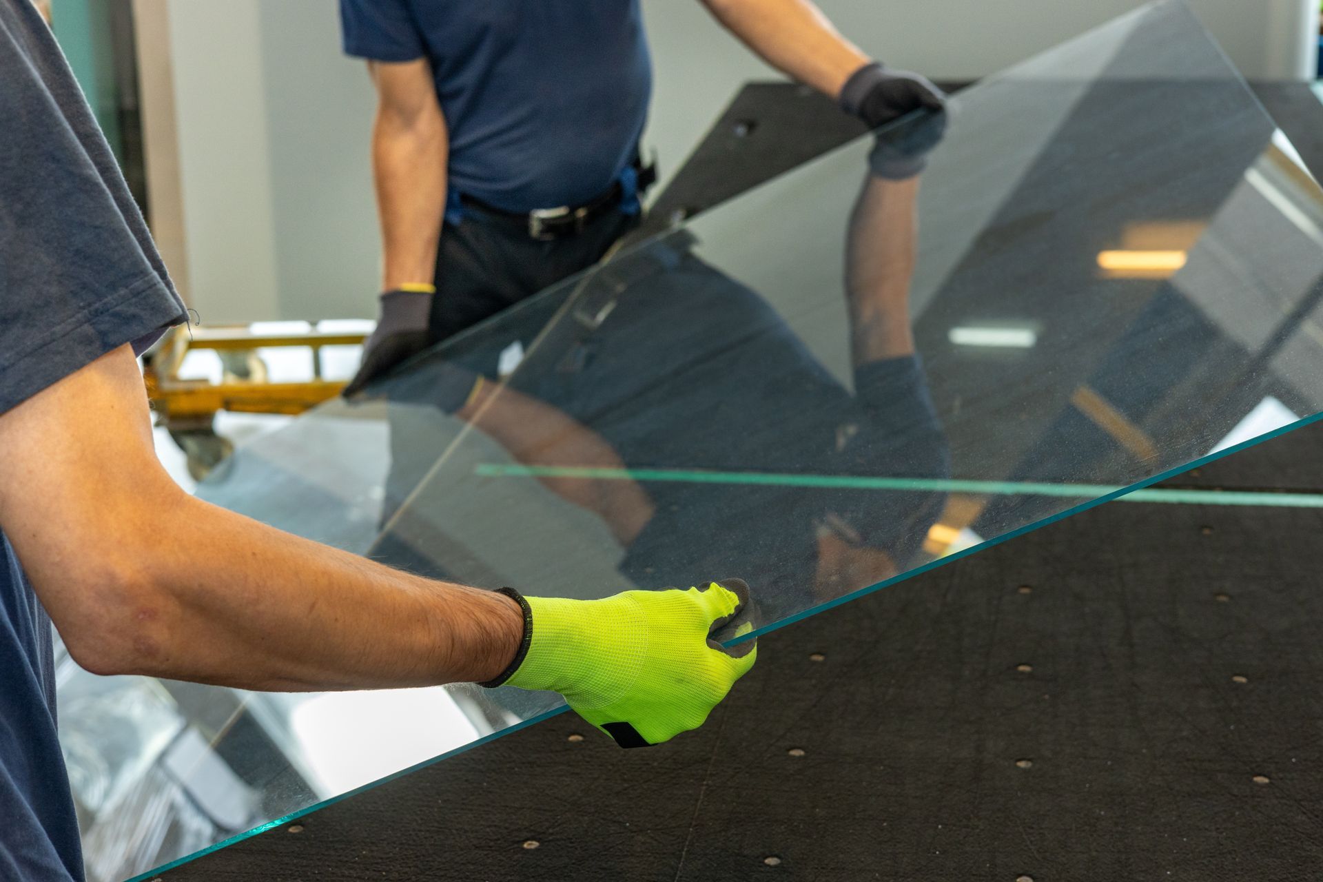 Workers in gloves handling a large glass pane in a workshop