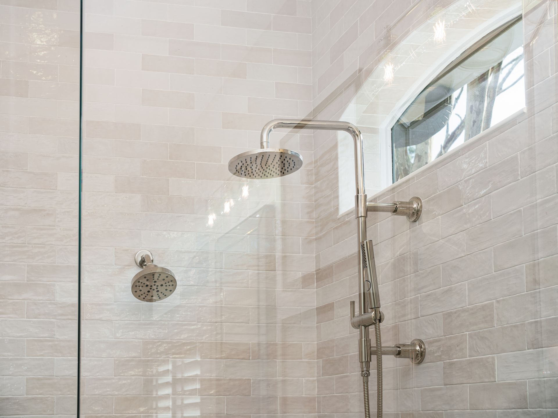 Walk-in shower with two showerheads, glass door, and white tile walls