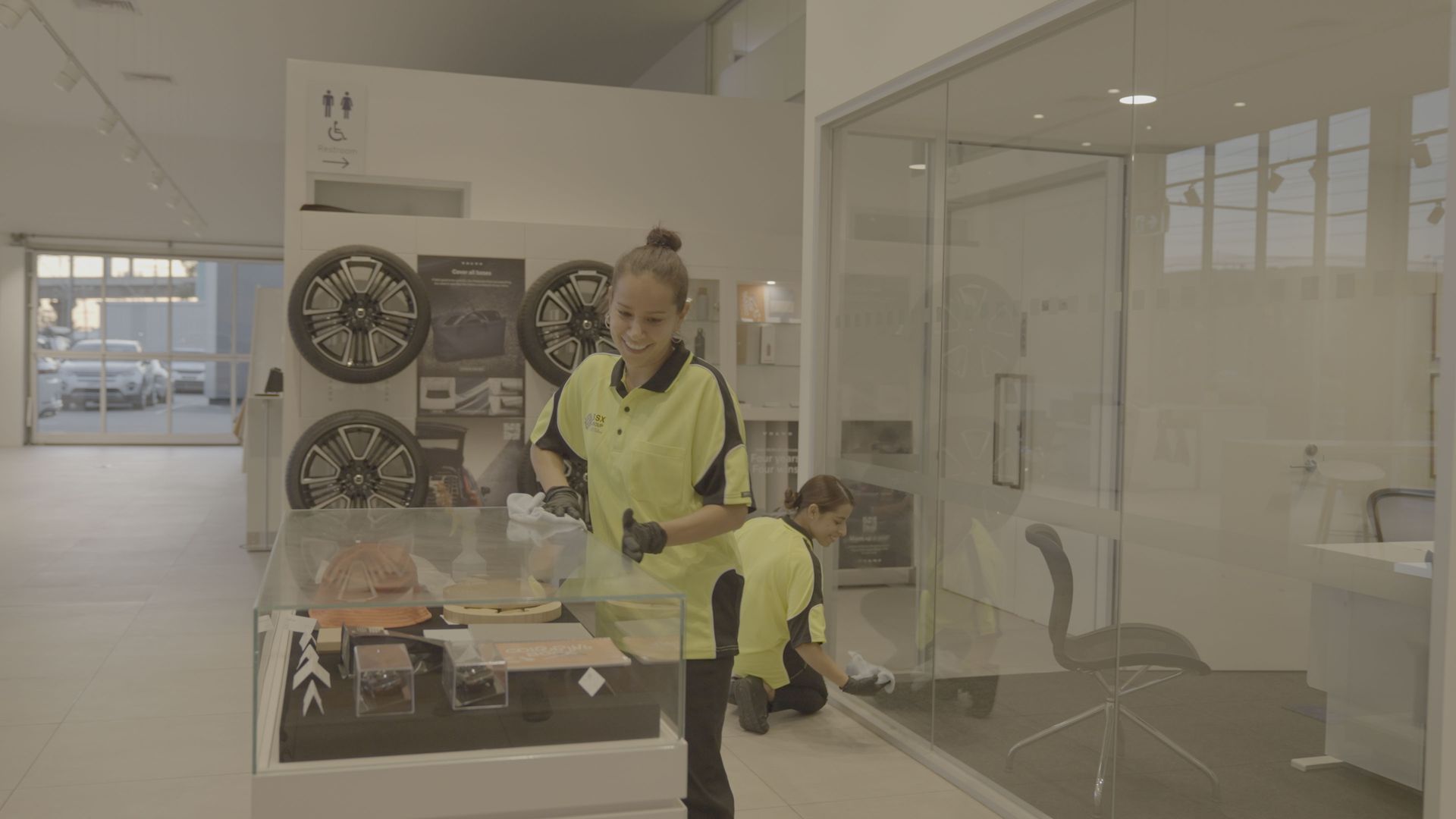 A woman in a yellow shirt is cleaning a glass table in a room.