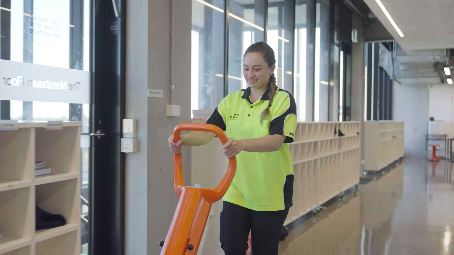A woman in a yellow shirt operates a vacuum cleaner, focused on cleaning the floor in a bright room.  