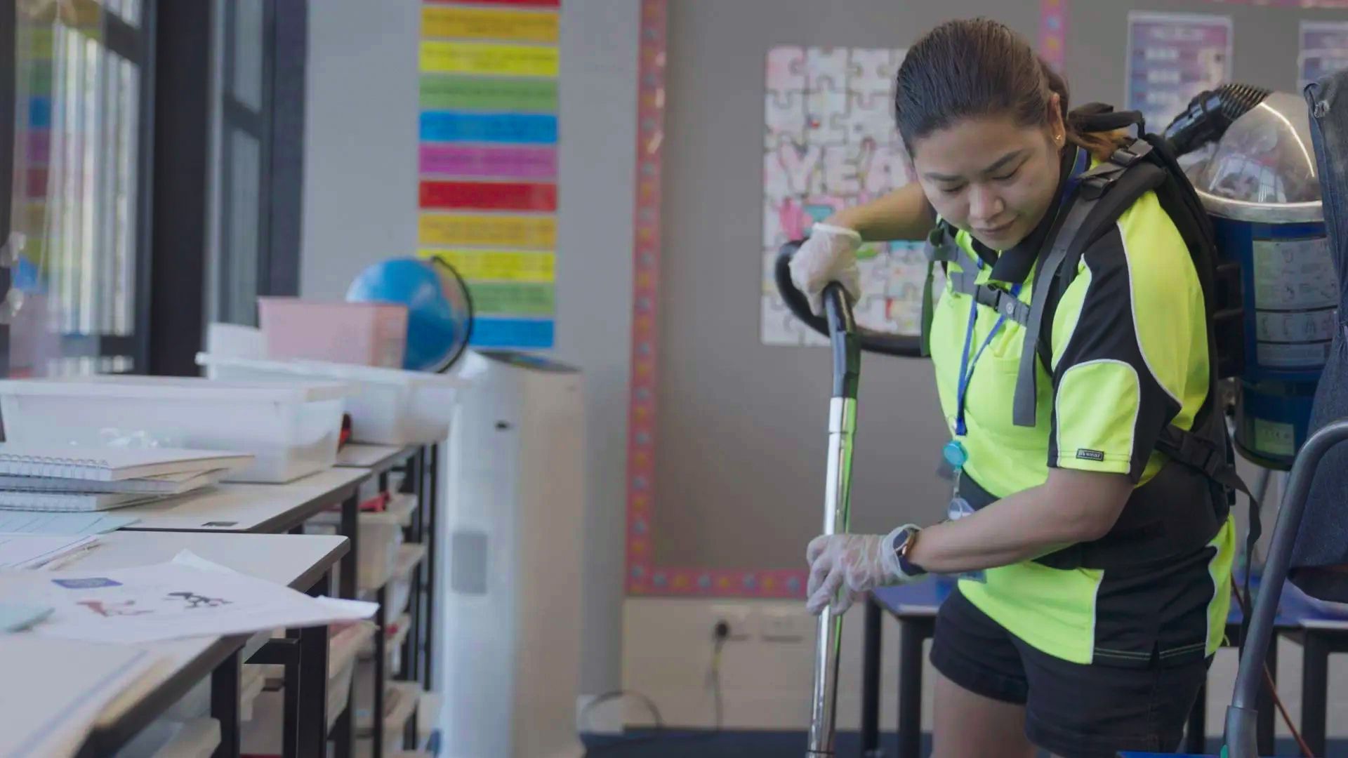 A woman is cleaning a classroom with a mop.