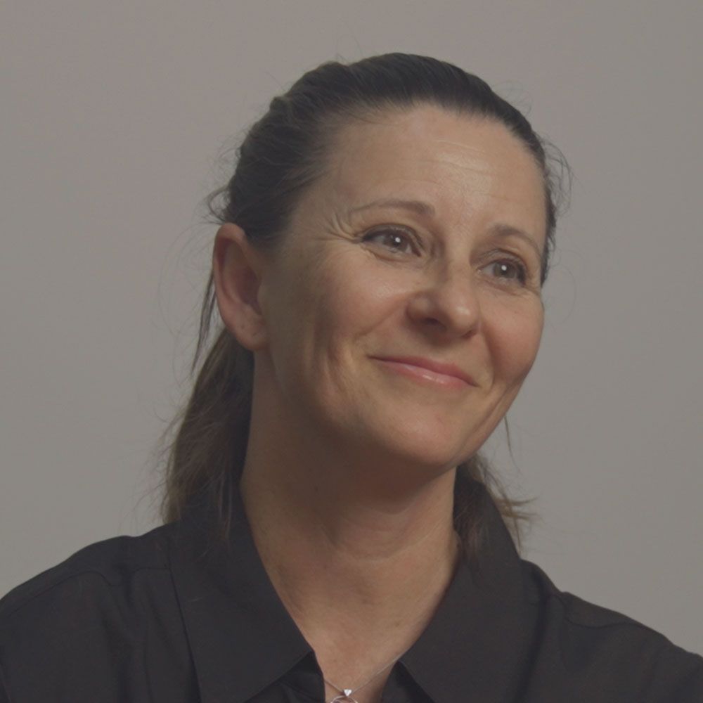 A woman wearing a black shirt and a necklace is smiling.