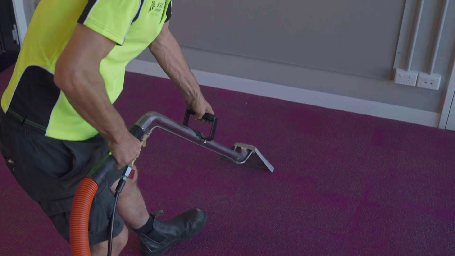 A Professional technician uses a carpet cleaning wand to deep-clean a purple commercial carpet