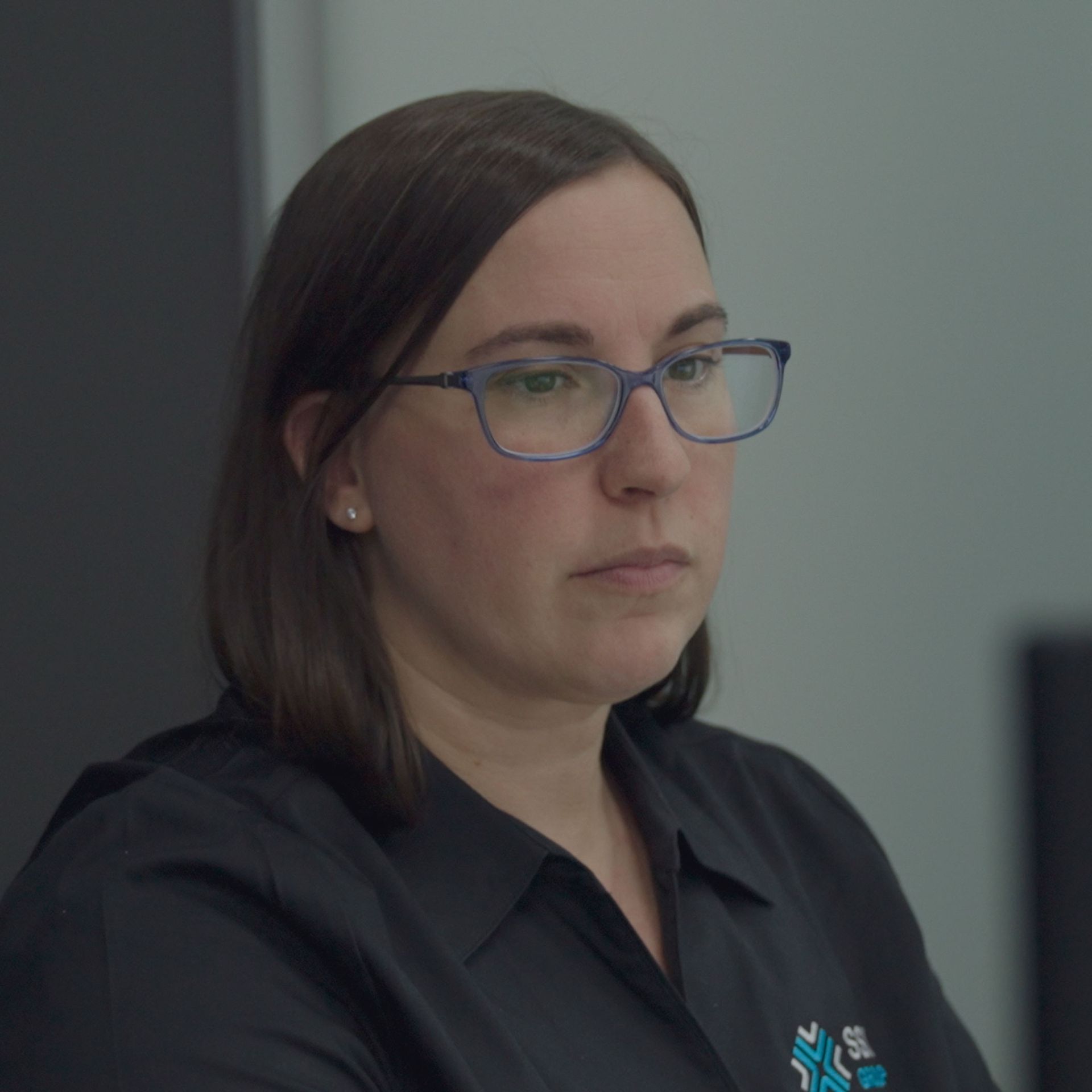 A woman wearing glasses and a black shirt is sitting in front of a computer.