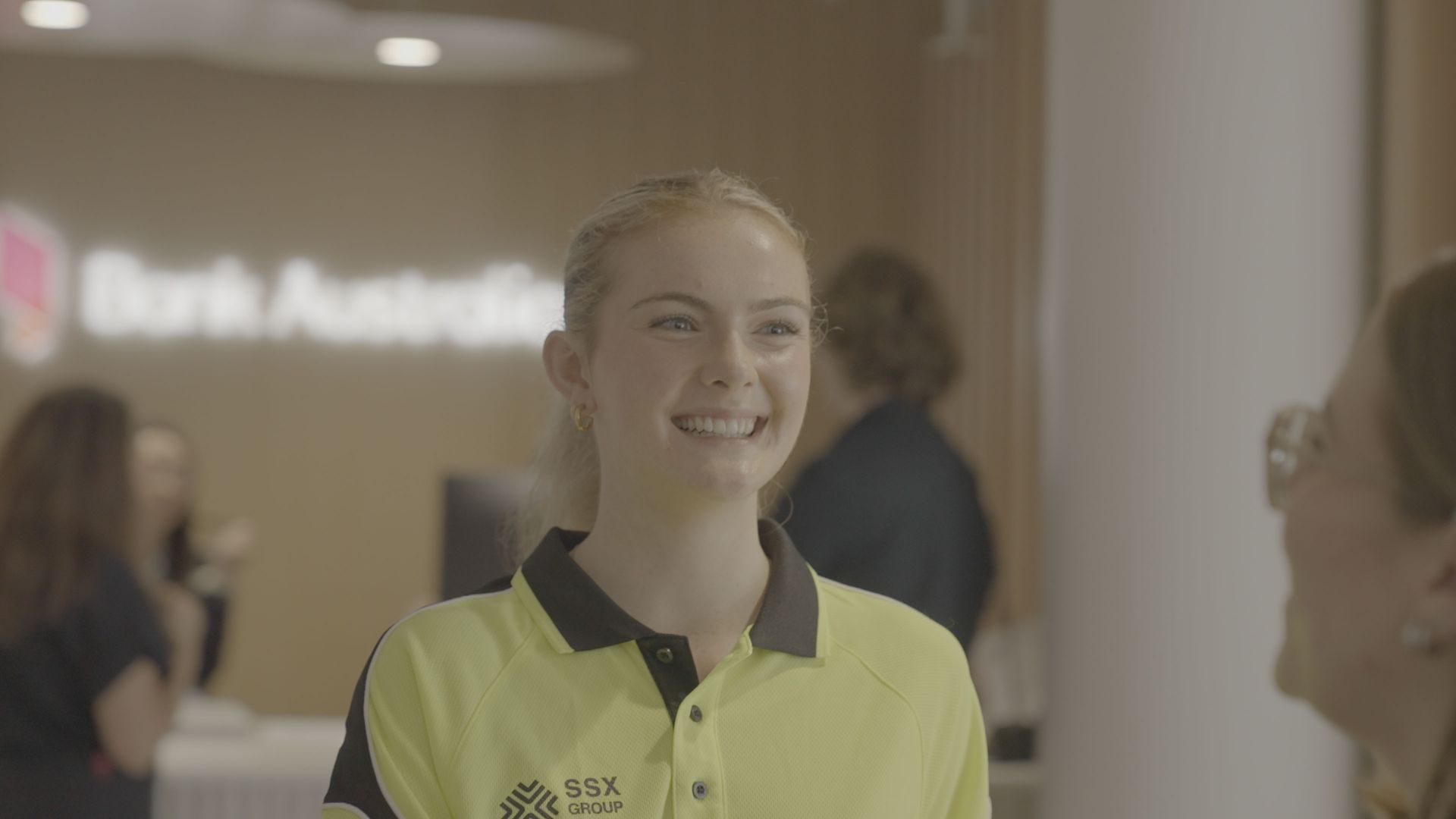 A woman in a yellow shirt is smiling in a bank.