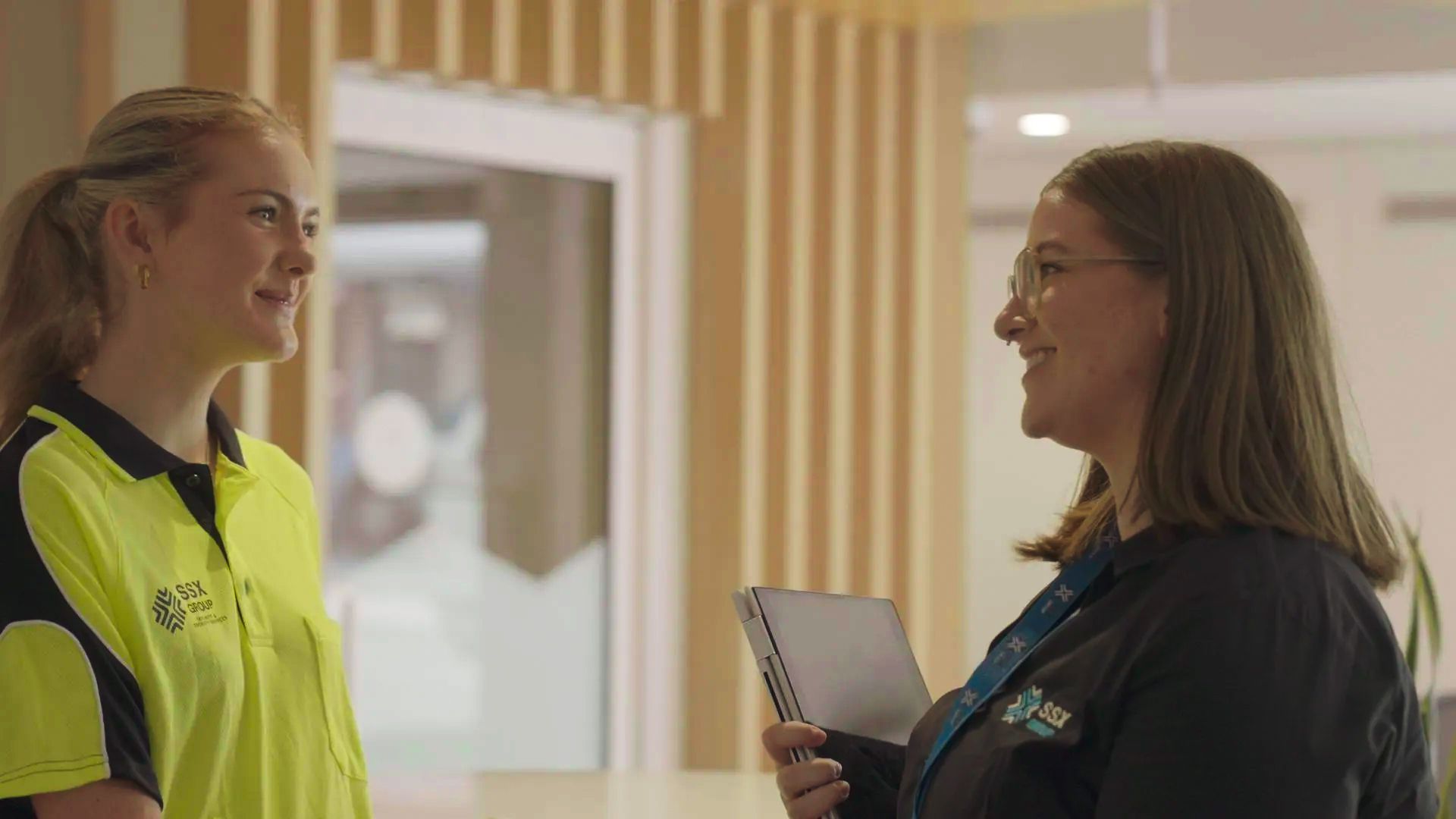 Two SSX Group women smile and talk to each other in a modern office. 