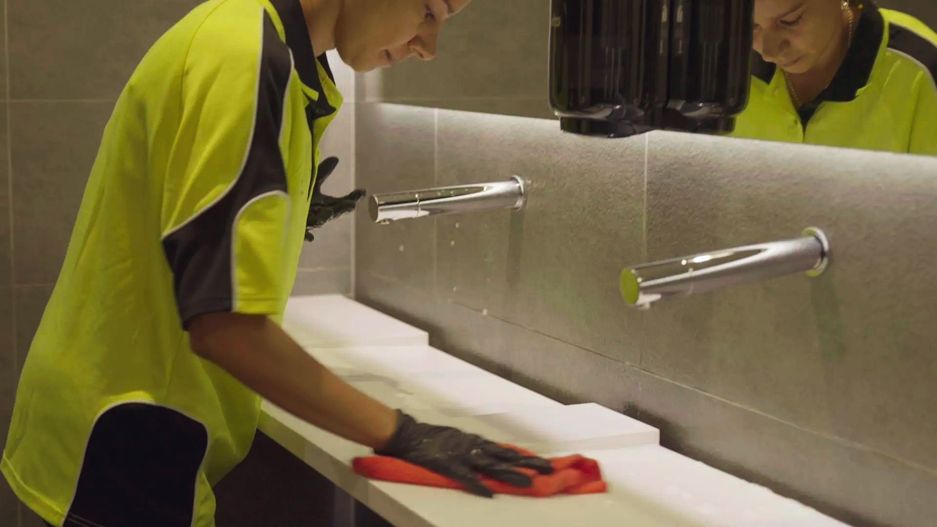 A woman is cleaning a bathroom sink with a cloth, which represents the SSX Group cleaning services