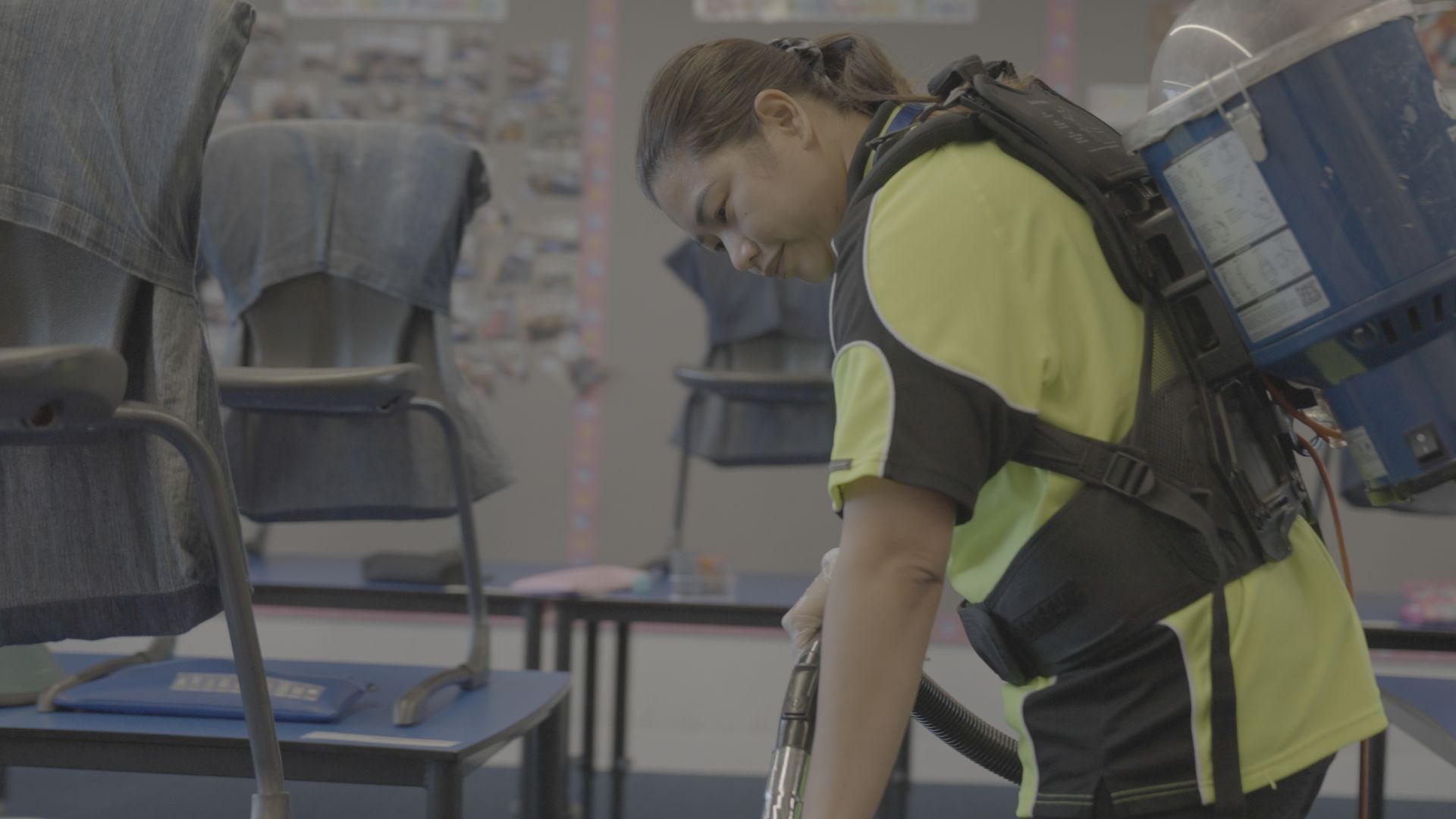A SSX group woman is cleaning a classroom with a vacuum cleaner.