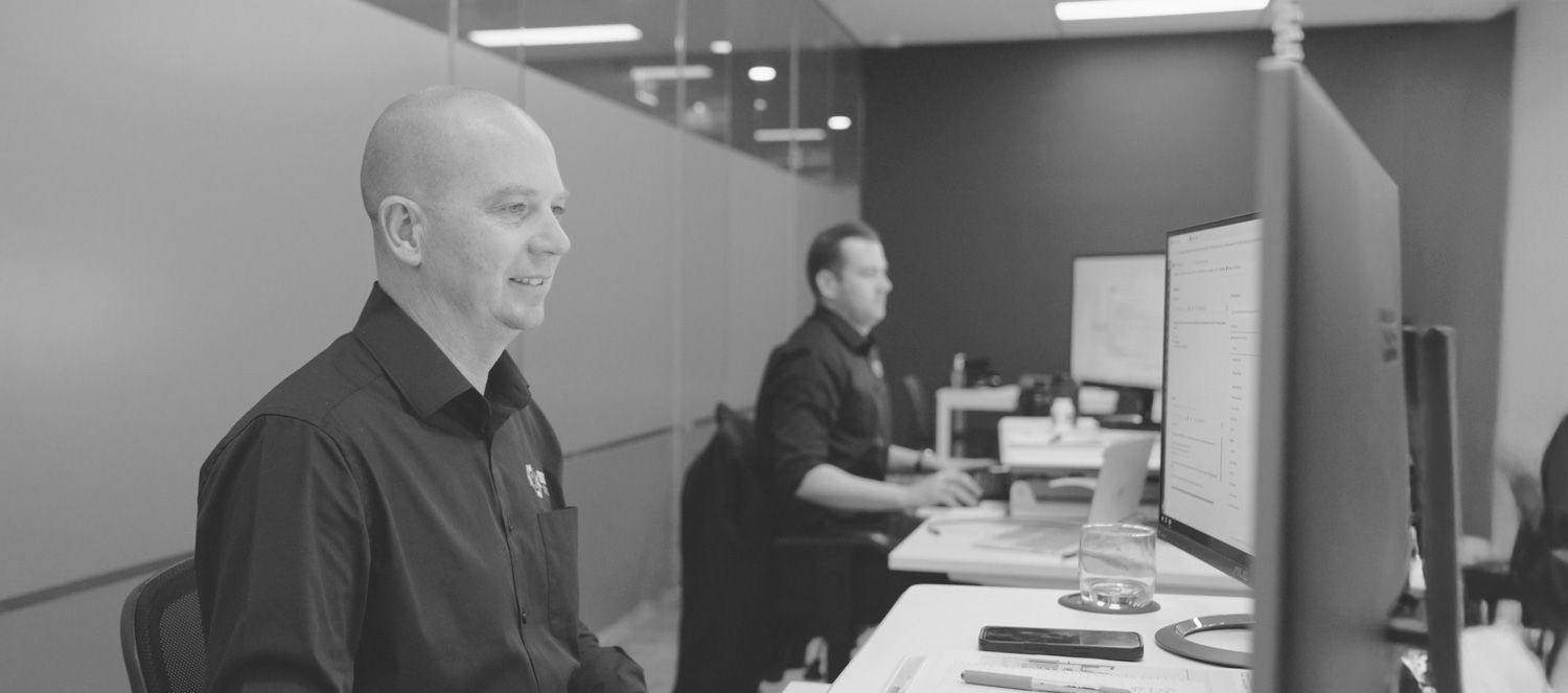 Two men seated at a desk, focused on their computers in the SSX group control room operations.