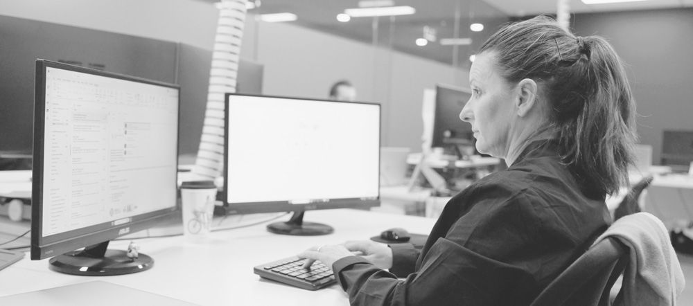 A woman is sitting at a desk in front of two computer monitors.