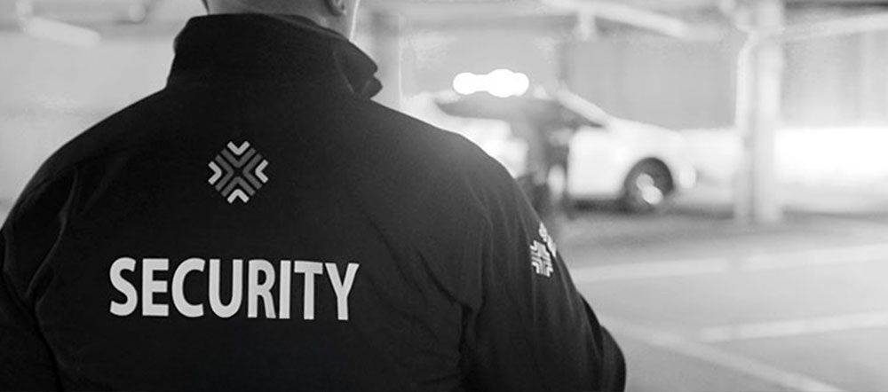 A security guard is standing in a parking garage looking at a car.