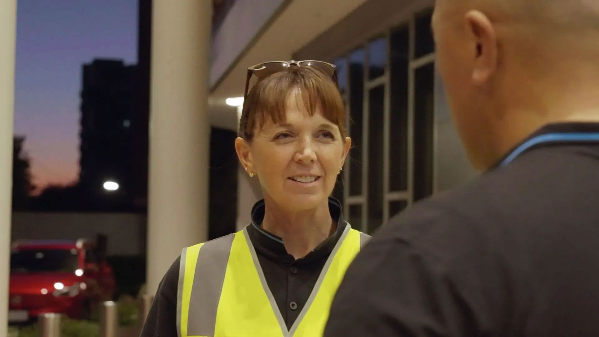 A woman in a safety vest smiles while talking to a man, representing SSX group security personnel in conversation.  