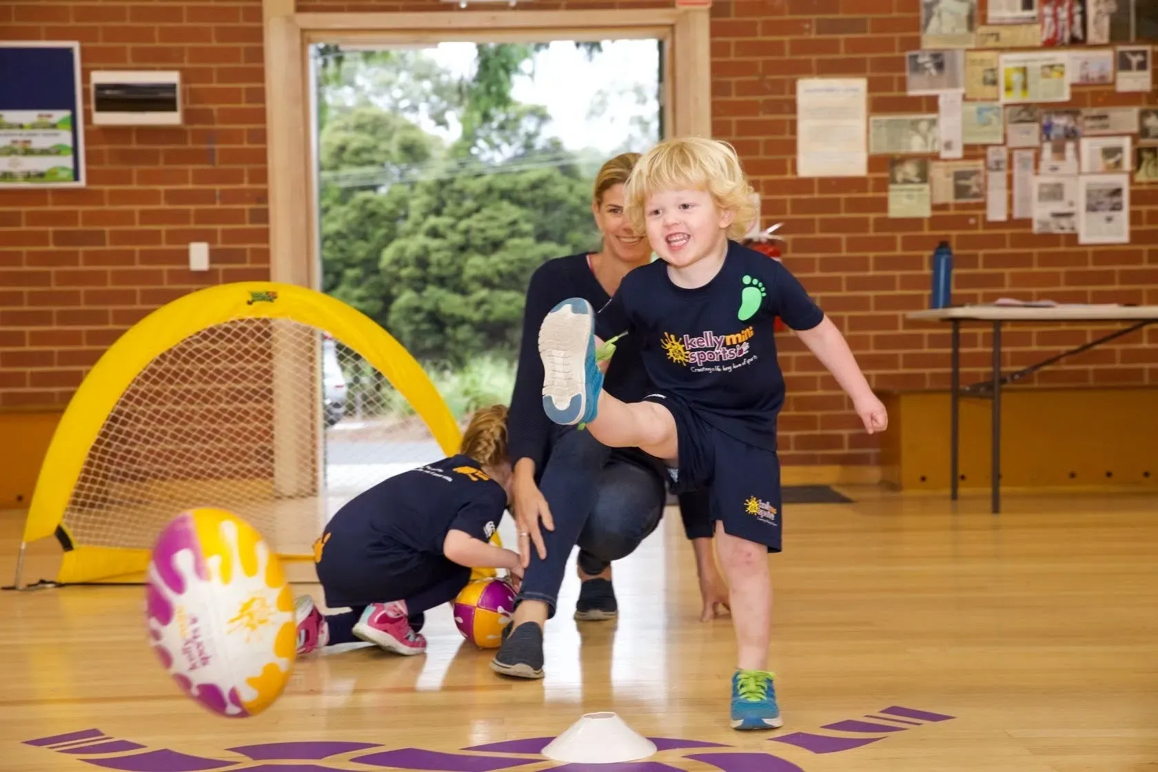 Children running through a gym obstacle course with a ball and cone on the floor